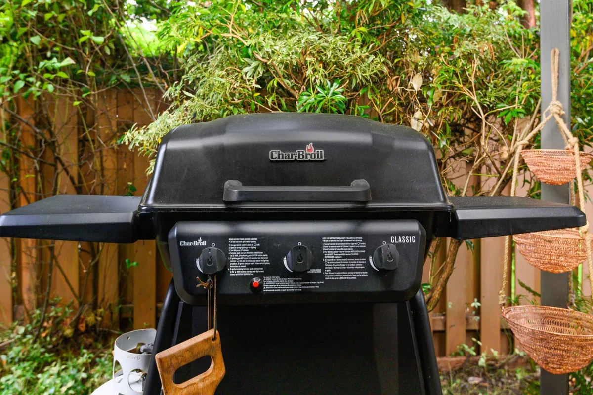 A relaxed backyard scene with a grill, wooden spatula, and lush greenery in the background, suggesting a setting perfect for family barbecues, outdoor dining, and casual gatherings.