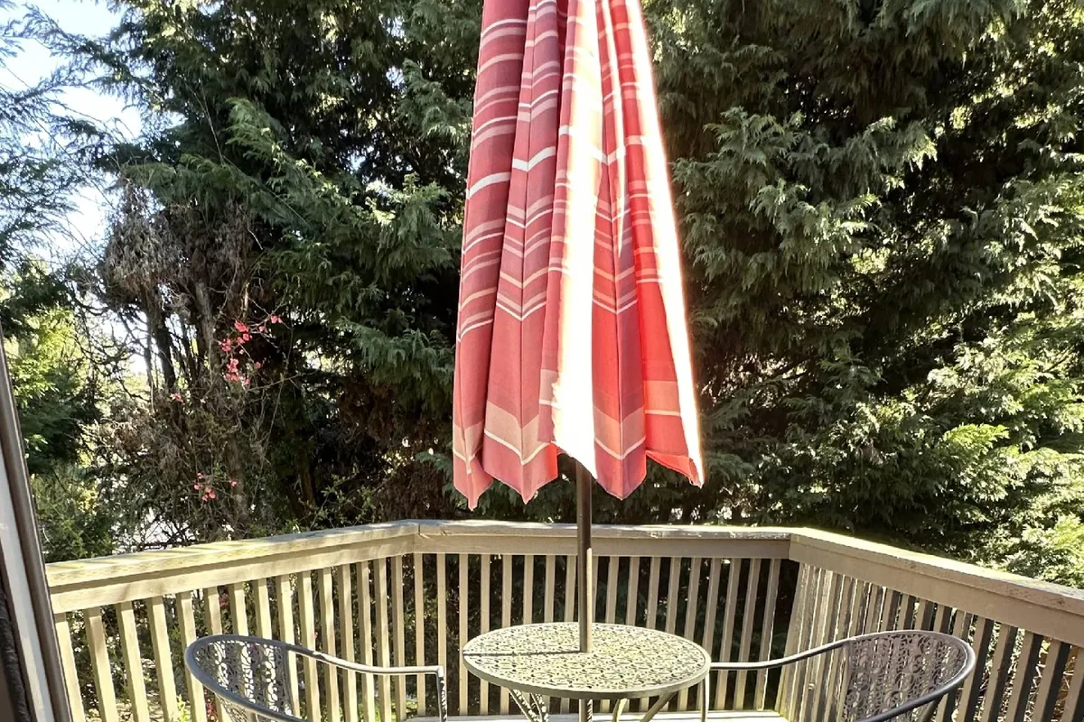 This image captures an inviting outdoor dining scene with a red umbrella shading a circular table surrounded by black metal chairs. The area is bathed in natural light, suggesting a perfect spot for socializing, enjoying meals, or unwinding after exploring the neighborhood.