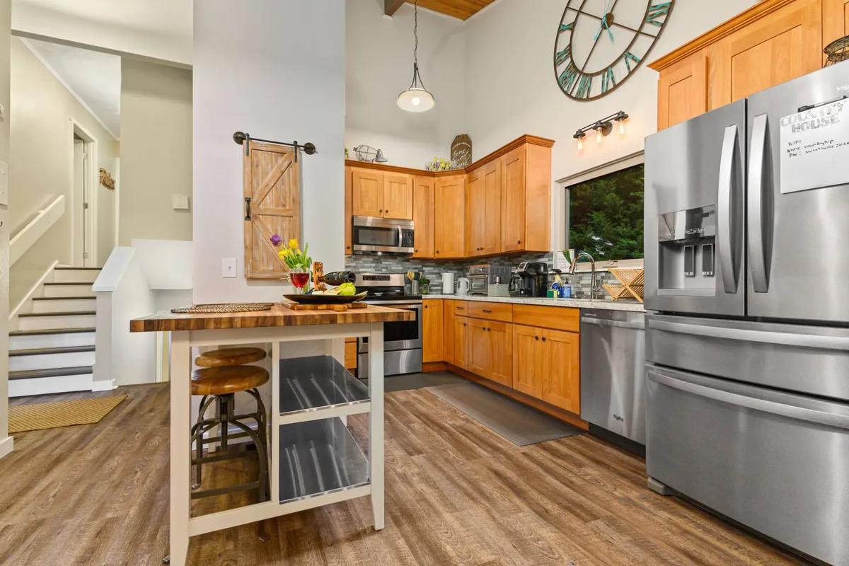 The kitchen island takes center stage with stainless steel appliances and wooden cabinetry, all under the glow of abundant natural light. The space is clearly set up for hosting, cooking, and bringing people together, with a warm and inviting mood.