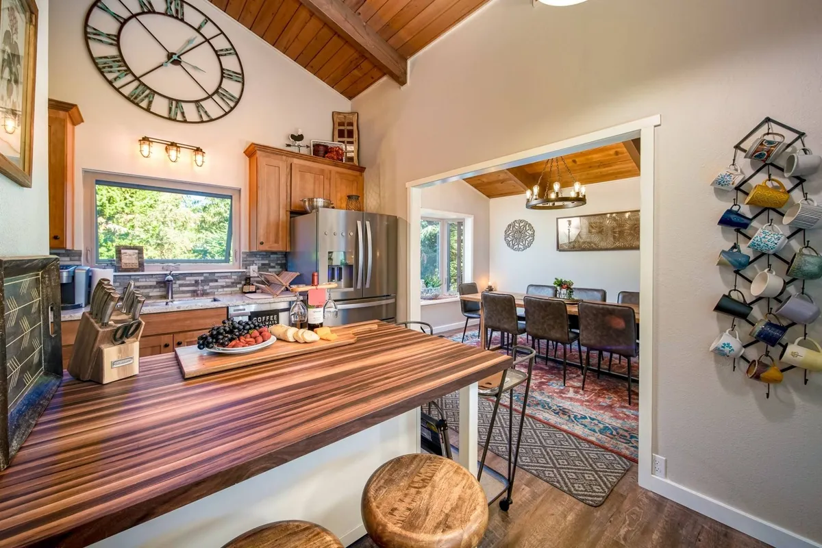 A warm, welcoming interior space featuring a wooden bar counter, cooking utensils, a dining area, and a colorful mug display. The setup encourages communal cooking, dining, and socializing.
