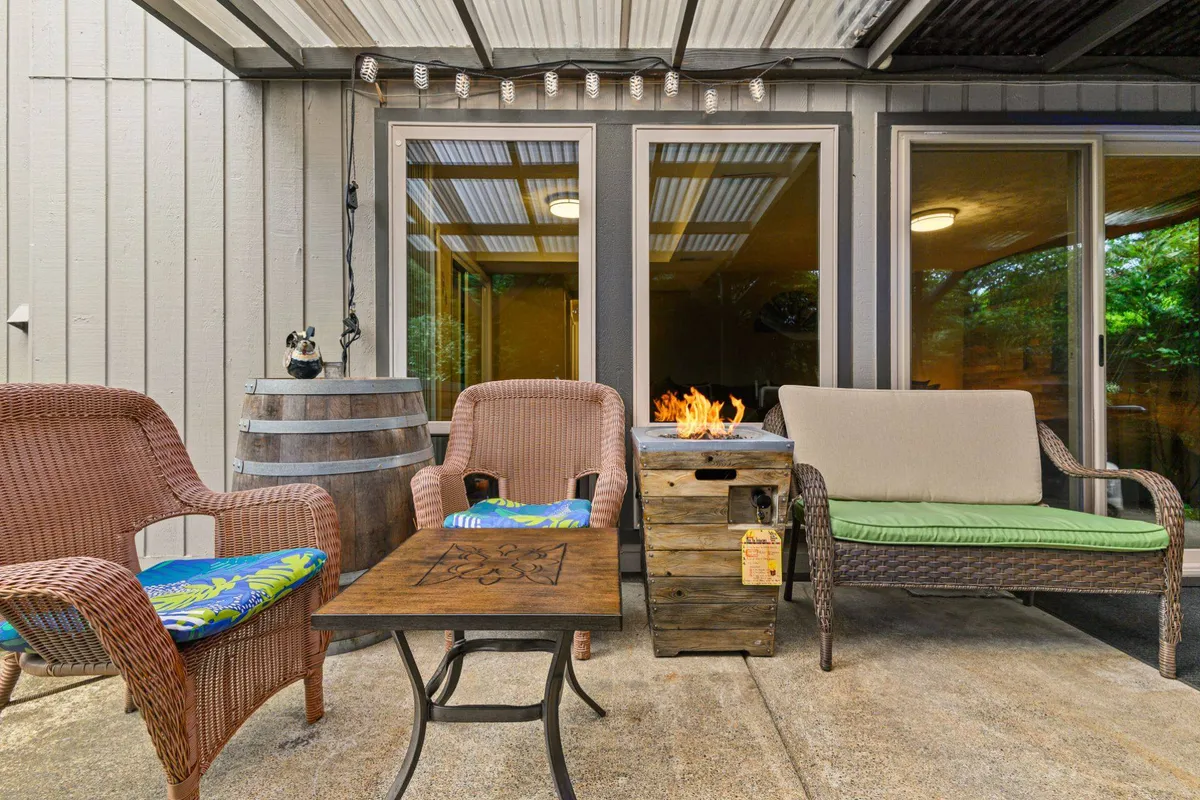 This exterior image showcases a backyard seating area featuring a fire pit surrounded by wicker chairs and a decorative table. The space is landscaped and inviting, ideal for families to gather in the evenings or enjoy a picnic outdoors under the pergola.
